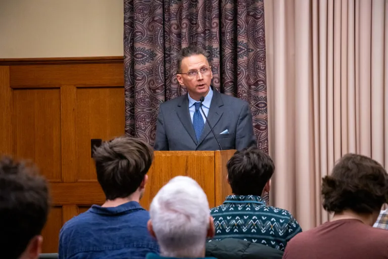 Krister Knapp stands at a podium presenting his lecture on the Monroe Doctrine, Trump, and Venezuela. Image by Hannah Dorval.