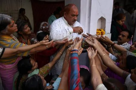 "The image appears to show Indian Hindu devotees with their hands raised to receive holy offerings or prasad inside a temple."