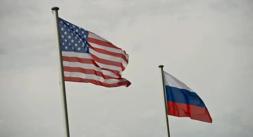 "The image shows the national flags of the United States and the Russian Federation flying outdoors against a cloudy sky."