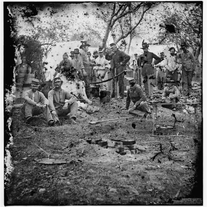 "Black and white photo from the civil war, cooking around a fire"