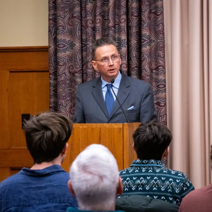 "Krister Knapp stands at a podium presenting his lecture on the Monroe Doctrine, Trump, and Venezuela. Image by Hannah Dorval."
