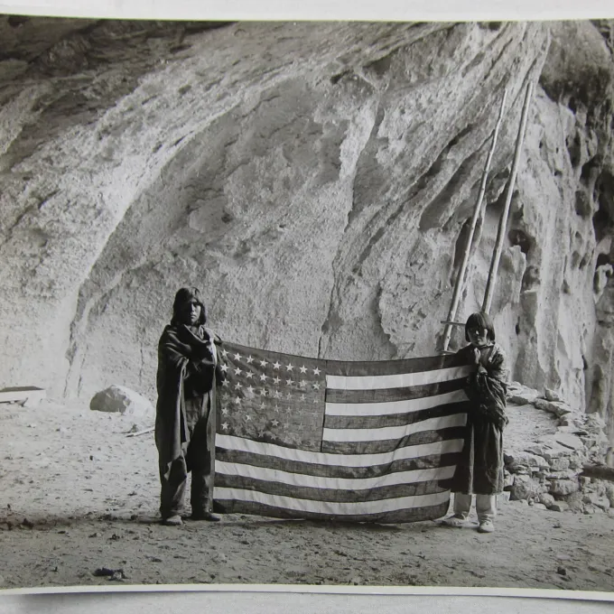 "Two Pueblo individuals hold an American flag, an image from the early 1900s."