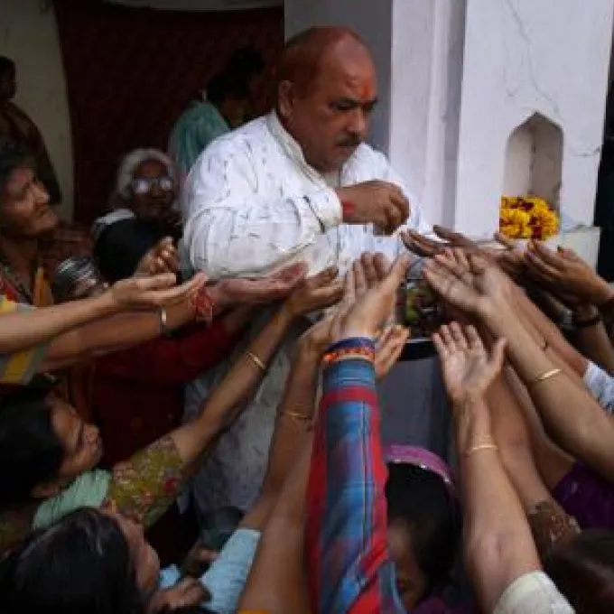 "The image appears to show Indian Hindu devotees with their hands raised to receive holy offerings or prasad inside a temple."