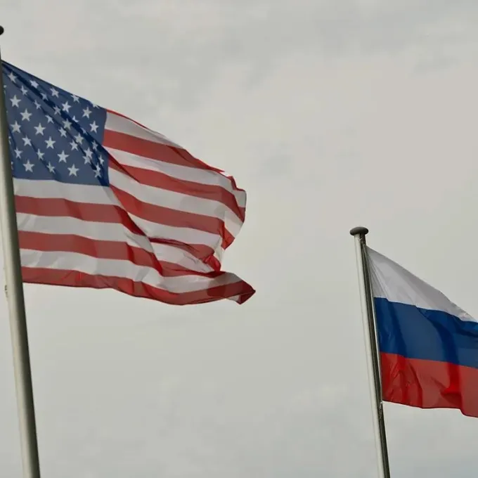 "The image shows the national flags of the United States and the Russian Federation flying outdoors against a cloudy sky."